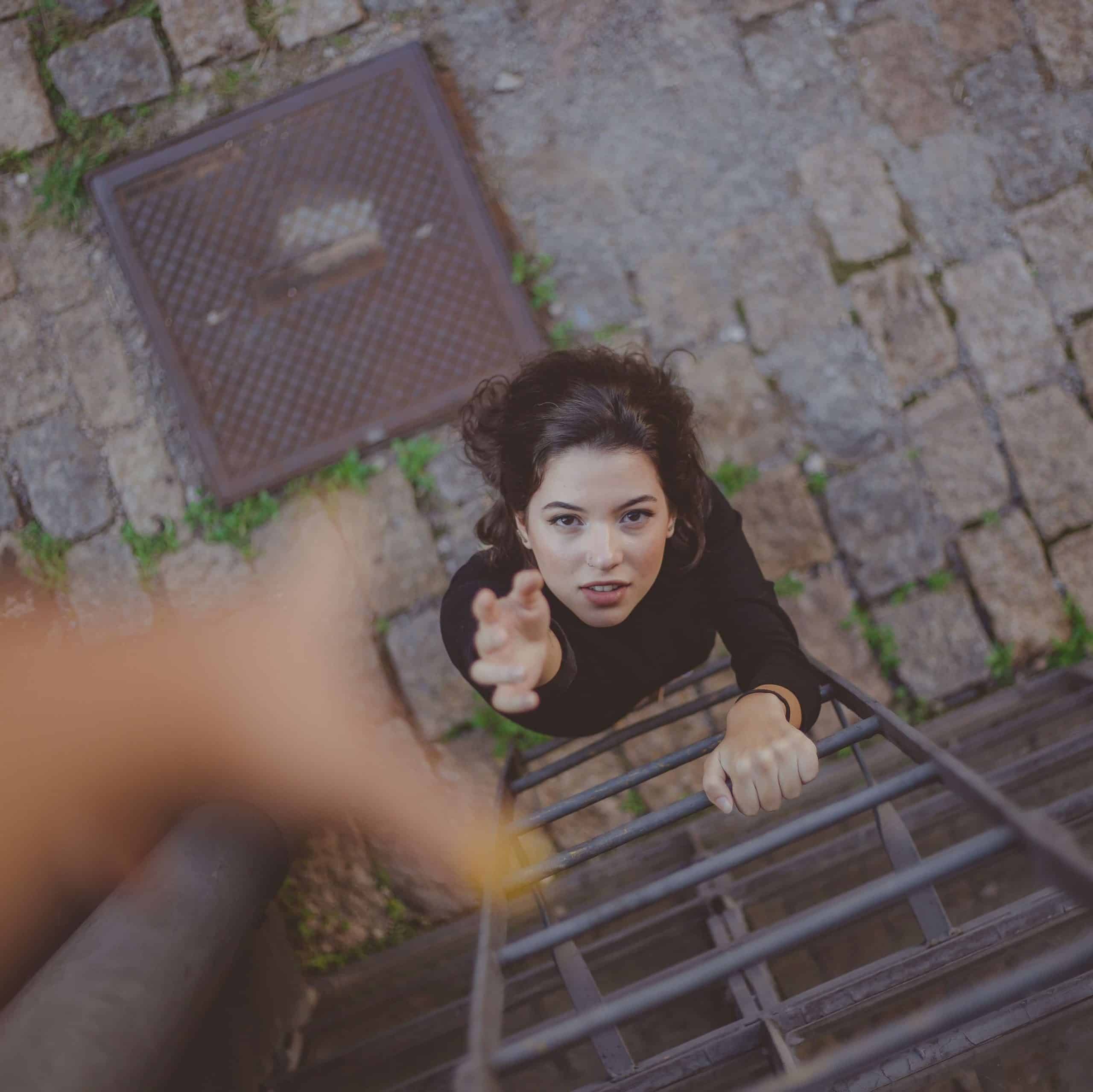 Maladaptive Schemas: Self Sacrifice: woman on a ladder reaching her hand up to someone for help